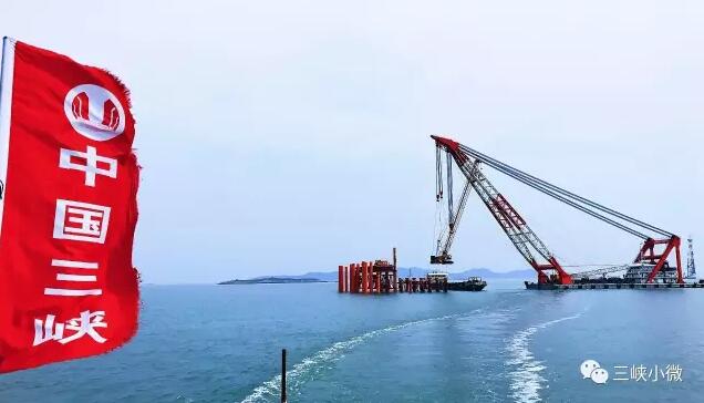 碧空如洗，白云低垂，海上一派風(fēng)平浪靜的景象。不遠(yuǎn)處兩臺已經(jīng)完成吊裝的風(fēng)機(jī)矗立海面，潔白的機(jī)身格外醒目